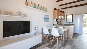 Une cuisine moderne avec des meubles blancs, un coin repas avec des chaises blanches, un téléviseur à écran plat et un tableau accroché au mur.