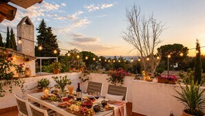 Un espace de restauration en plein air avec une table dressée pour un repas, entouré de plantes en pot et illuminé de guirlandes lumineuses.