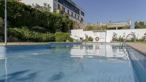 Une piscine aux eaux claires, agrémentée d’un panneau indiquant qu’il est interdit de plonger, entourée de verdure et avec un bâtiment visible au loin.