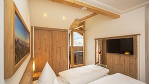 Un dormitorio con paredes de madera, una cama, televisor montado y ventana con vista a una montaña.