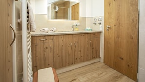 Un baño con armarios de madera, un lavabo con espejo y una ducha.