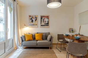 A living room with a grey sofa, yellow cushions, a dining table with chairs, and two posters on the wall.