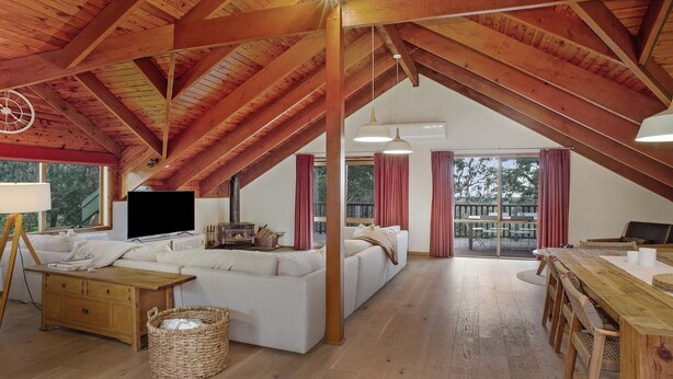 Un loft spacieux avec de hauts plafonds, des poutres apparentes, un grand canapé, une télévision et une cheminée.
