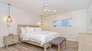 A bedroom with a wooden bed, a nightstand, a bench, a ceiling fan, and a window. - Luxury Villa - Studio I (Carlsbad)