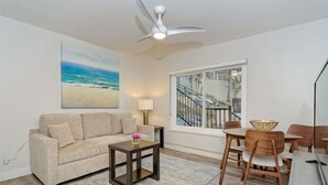 A living room with a beige sofa, a small wooden coffee table, a lamp, and a dining area with wooden chairs and a table. - Luxury Villa - Studio I (Carlsbad)