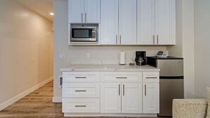 A compact kitchen with white cabinets, a microwave, a coffee maker, and a refrigerator. - Luxury Villa - Studio I (Carlsbad)