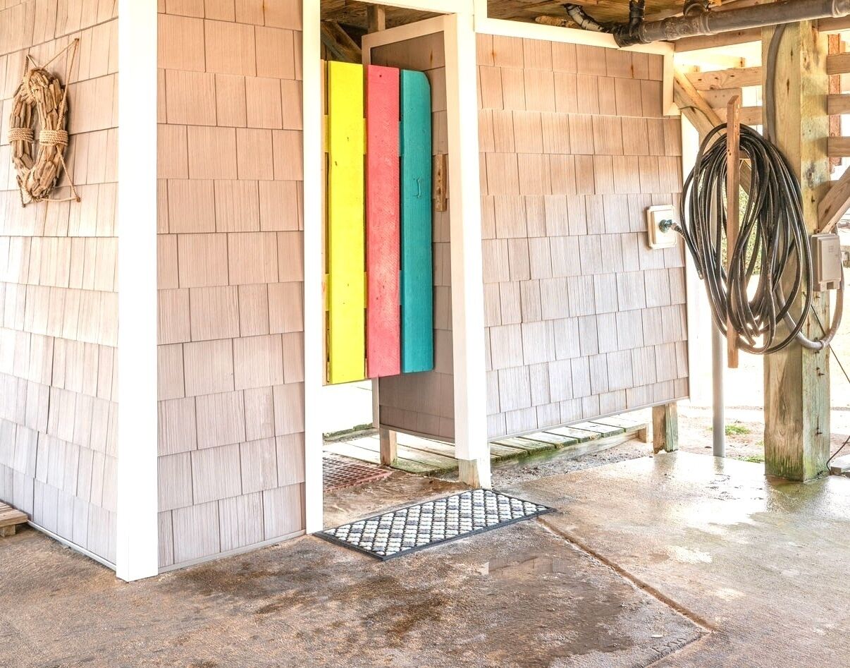 A covered outdoor area with wooden siding, a colorful vertical panel, and a coiled hose on a wooden post.