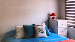 A bedroom with a bed, a ceiling fan, a nightstand with a lamp, and a window with blinds.