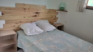 Een slaapkamer met een houten hoofdbord, twee nachtkastjes, een bed met een dessin en een kleine groene lamp op een plank.