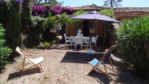 Een terras met een tafel en stoelen, omringd door planten en een pergola met paarse bloemen.