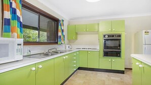 A kitchen with green cabinets, a white microwave, a double oven, and a window with colorful curtains. - Backs Directly Onto Leura Golf Course (LEURA)