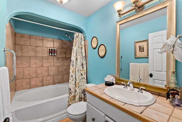 Un baño con bañera, inodoro, lavabo y un espejo grande.