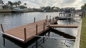 Un muelle de madera se adentra en aguas tranquilas, rodeado de palmeras y una hilera de casas.
