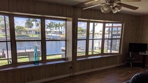 Una habitación con amplios ventanales que dan a una piscina y un campo de golf, paredes de madera, un ventilador de techo y un mueble para televisor.