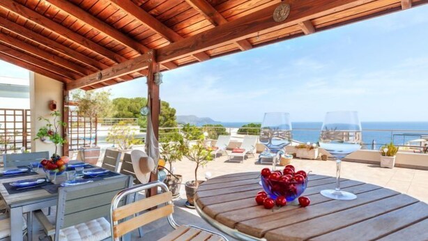 Un área de comedor al aire libre cubierta con mesa para dos, una banca y vistas al mar.