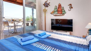 Habitación de hotel con cama, televisor, zona de comedor con sillas y una mesa, y vistas al exterior.