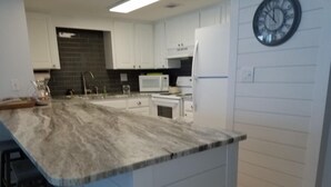 A kitchen with a marble countertop, white cabinets, a microwave, and a clock on the wall. - Island Sunrise, sleeps 6, 2 bed / 2 bath, GULF VIEW-beach side (Gulf Shores)