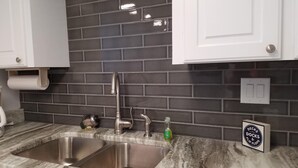 A kitchen with a stainless steel sink, dark tiled backsplash, and white cabinets. - Island Sunrise, sleeps 6, 2 bed / 2 bath, GULF VIEW-beach side (Gulf Shores)