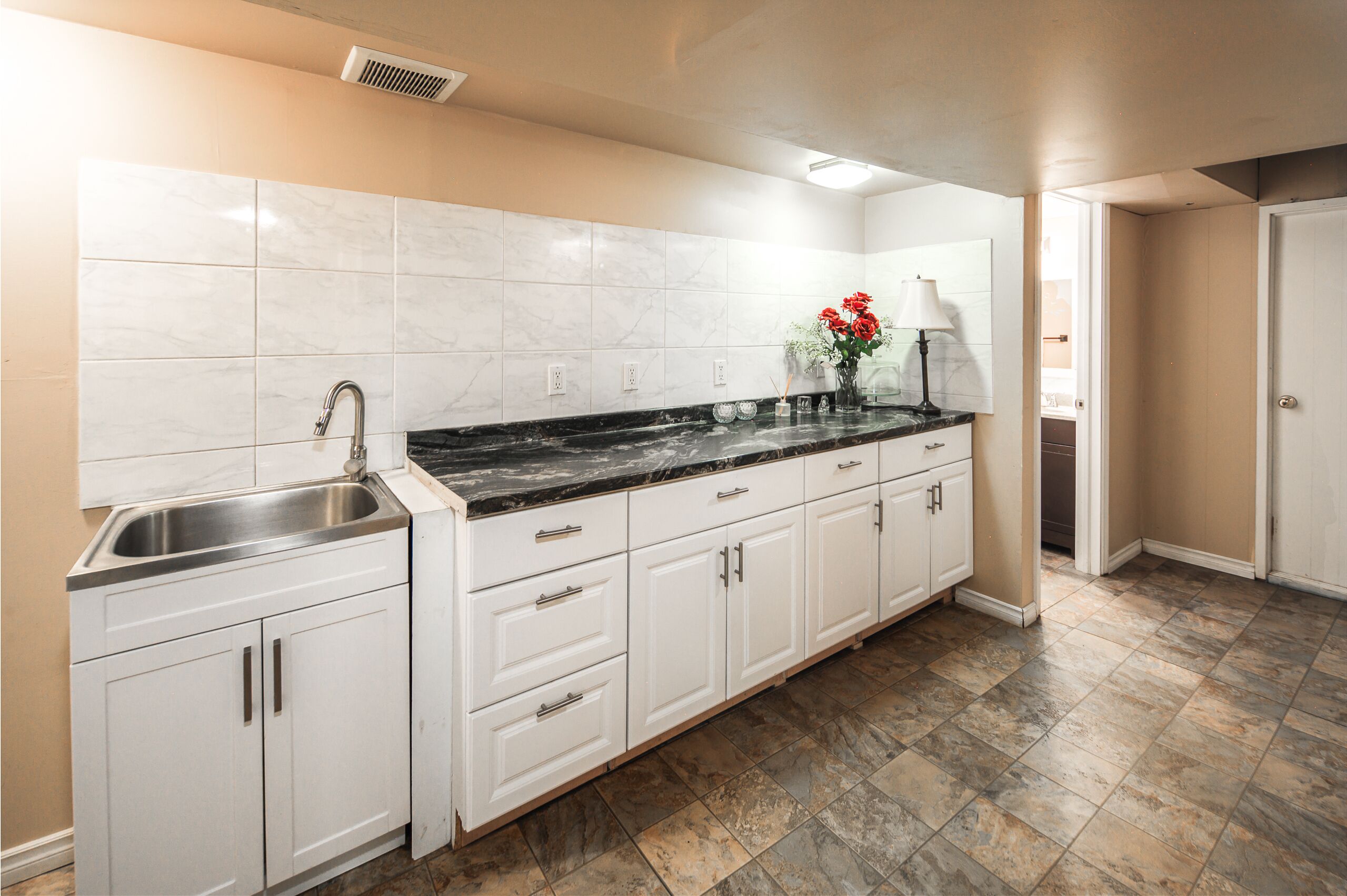 A kitchen with white cabinets, a black countertop, and a stainless steel sink.