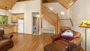Ein großzügiger Wohnbereich mit einer Holztreppe, Ledersofas und einer Küche im Hintergrund.