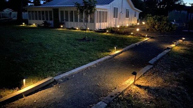 Une maison avec un toit en pente, une véranda et une cour bien éclairée, avec un chemin.