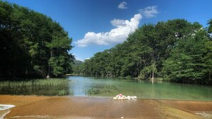 Une rivière bordée d’une forêt verdoyante et dense, une plage de sable et un ciel dégagé.