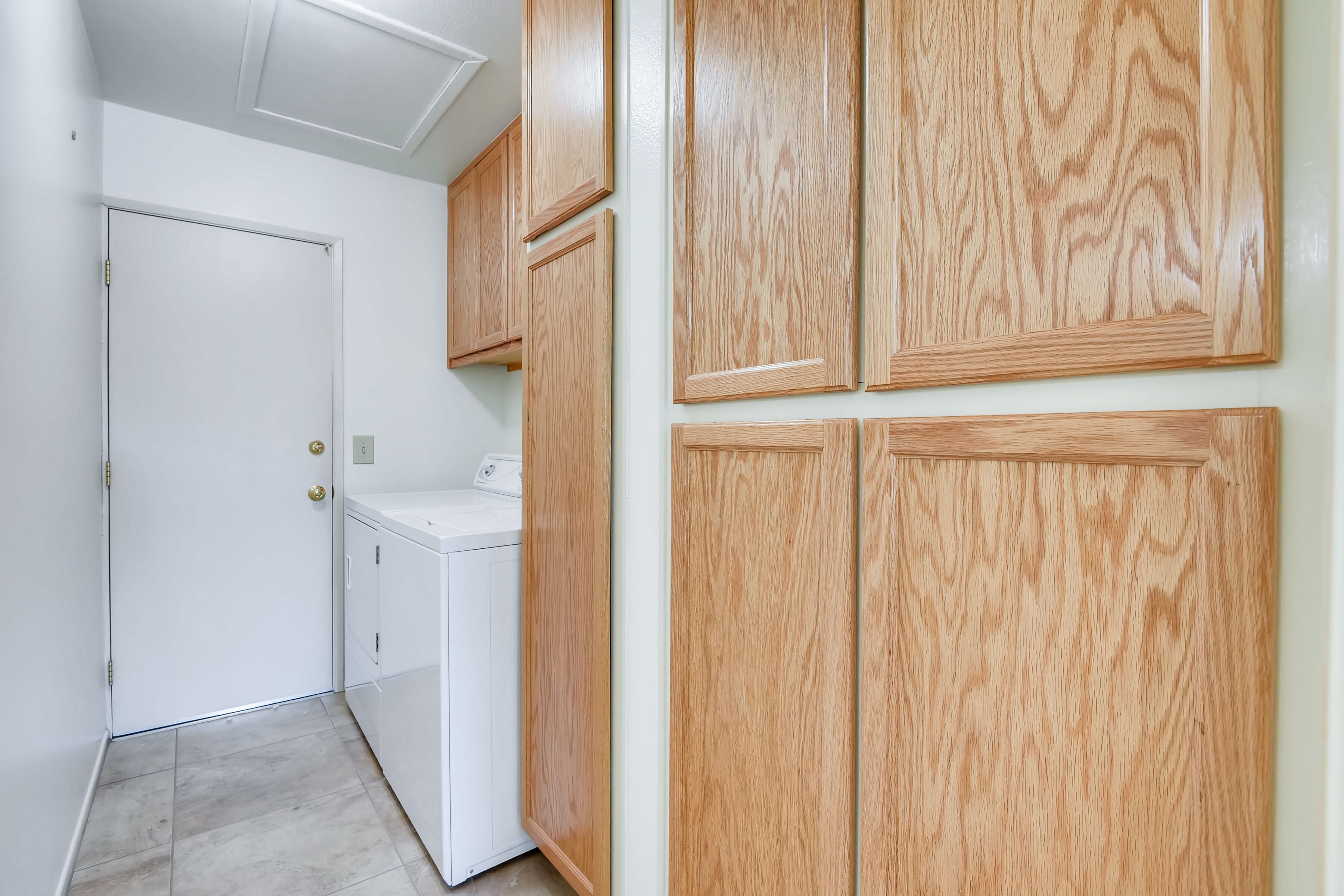 A laundry room with a white washing machine, wooden cabinets, and a door.