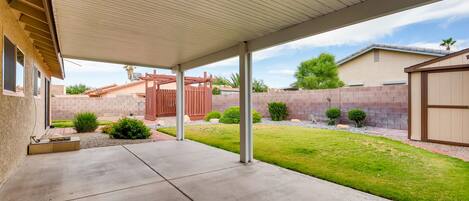A covered patio area with a concrete floor, a wooden fence, and a brick wall in the background.