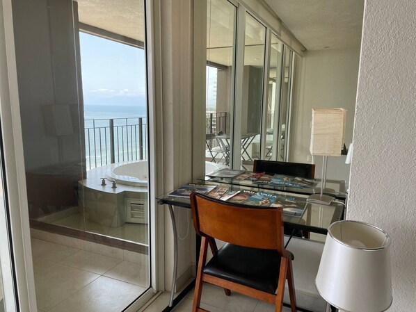 Une chambre moderne avec une table en verre, une chaise, une lampe et une vue sur l’océan grâce à de grandes fenêtres.