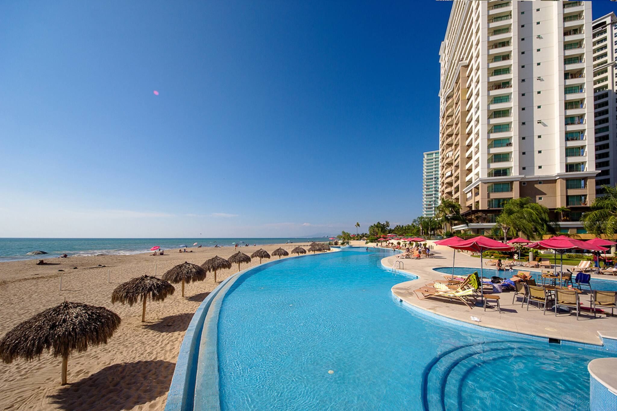 A resort pool with a beach and a high-rise building in the background.