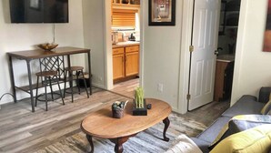 A living room with a wooden coffee table, a sofa, and a TV mounted on the wall. - Ravens Hideaway Cottage on Main, King, KItchen, Living Rm, w/d &  Patio w/Grill (Westcliffe)