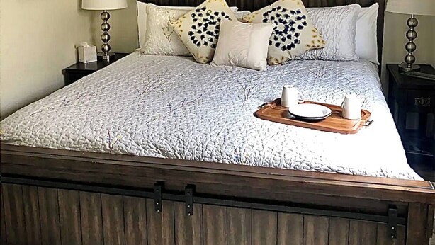 A bedroom with a wooden bed frame, a ceiling fan, and a sign on the wall. - Ravens Hideaway Cottage on Main, King, KItchen, Living Rm, w/d &  Patio w/Grill (Westcliffe)