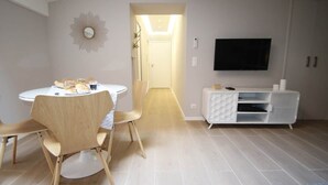 Una sala de estar moderna con una mesa redonda de comedor, sillas de madera, un televisor de pantalla plana y un mueble blanco.