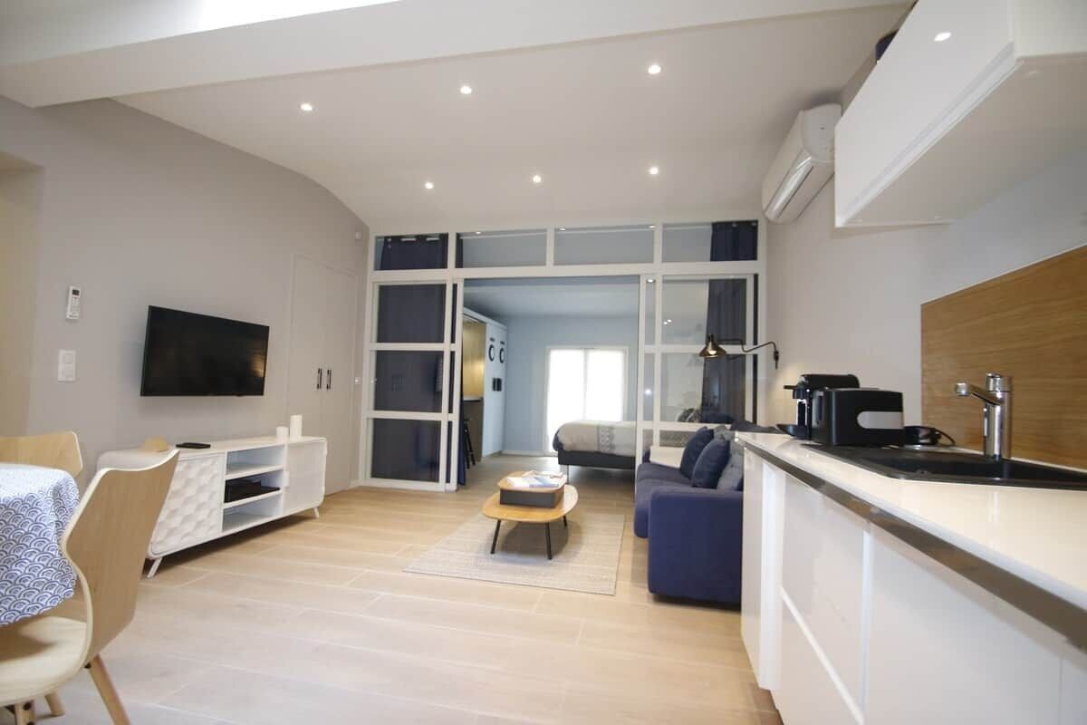 A modern living room with a sofa, a coffee table, a TV, and a kitchen area with a sink and counter.