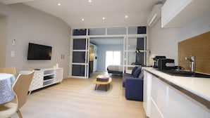 Una sala de estar moderna con un sofá, una mesa de centro, un televisor y una zona de cocina con un fregadero y encimera.