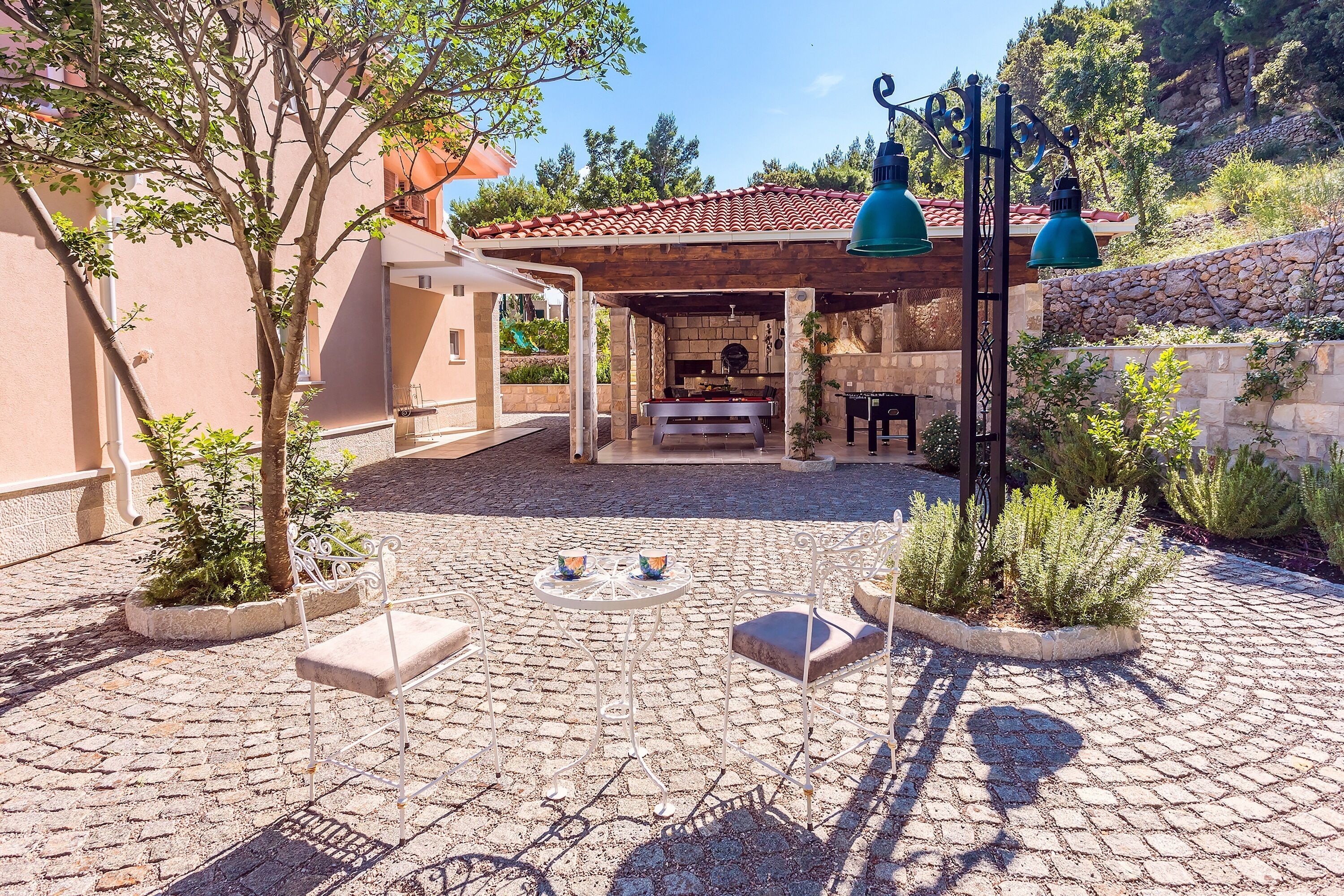 A courtyard with a stone floor, outdoor seating, a barbecue area, and a pergola with hanging lights.