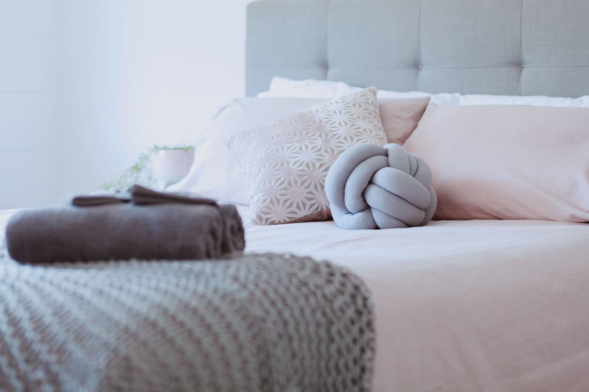 A neatly made bed with a grey knitted blanket, a decorative pillow, and a folded towel.