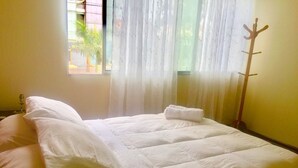 A neatly made bed with white linens, a wooden coat rack, and a window with sheer curtains. - "Your home in Miraflores" 4 pers (Lima)