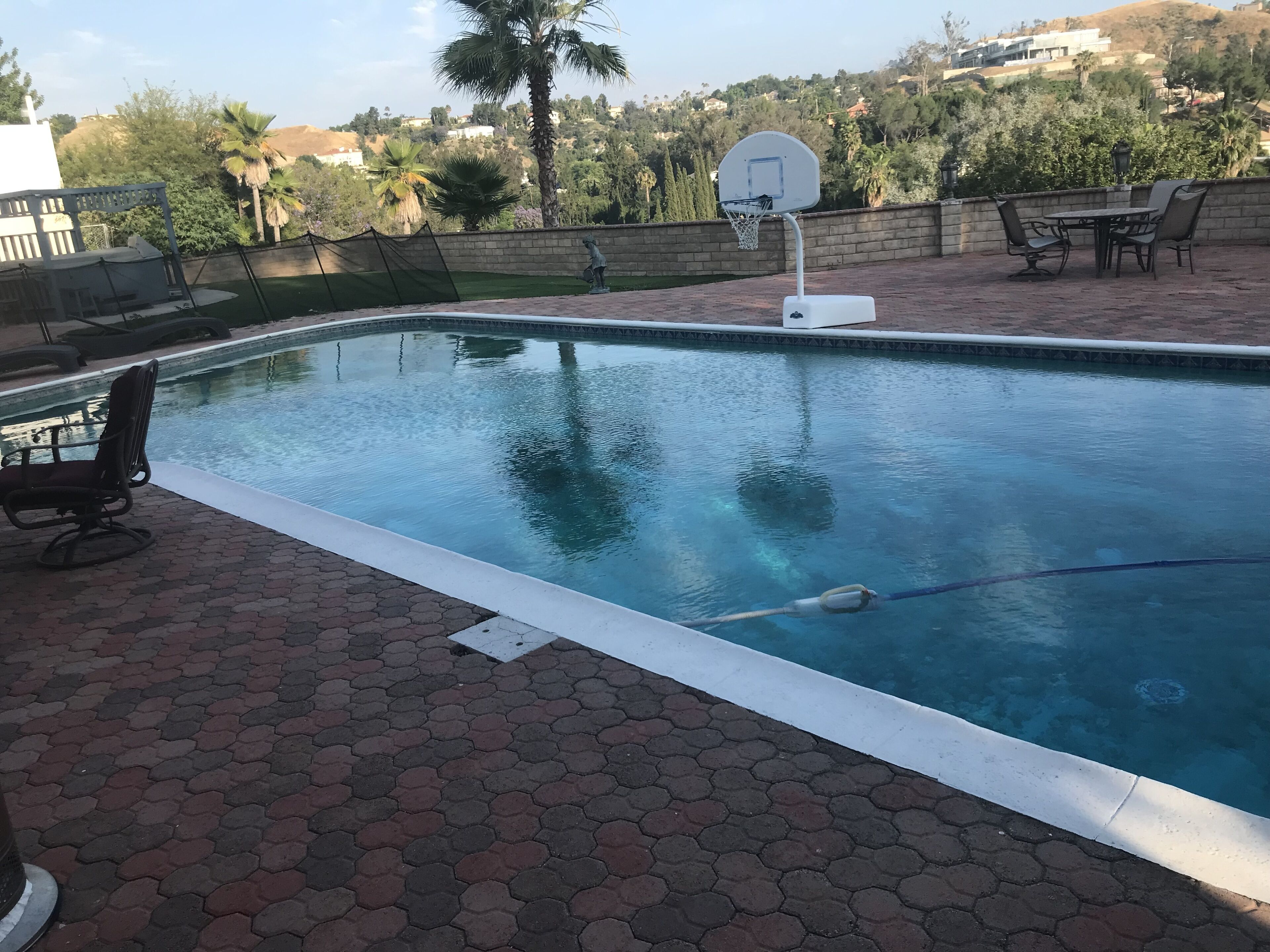 Una piscina con aro de baloncesto, una silla y una mesa.