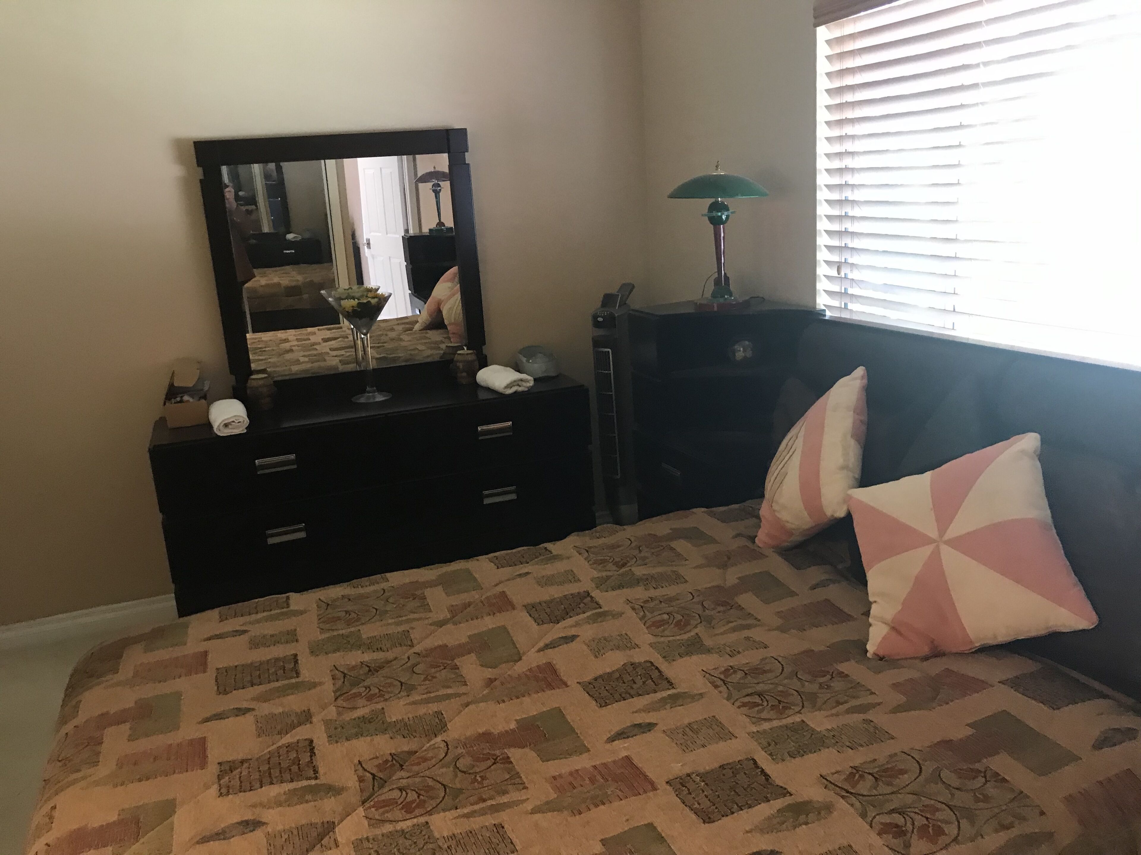 A bedroom with a bed, a dresser with a mirror, a lamp, and a window with blinds.