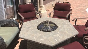 Eine Terrasse mit Steintisch und zwei Stühlen, einem dekorativen Löwenkopf und einem Fenster mit Vorhängen.