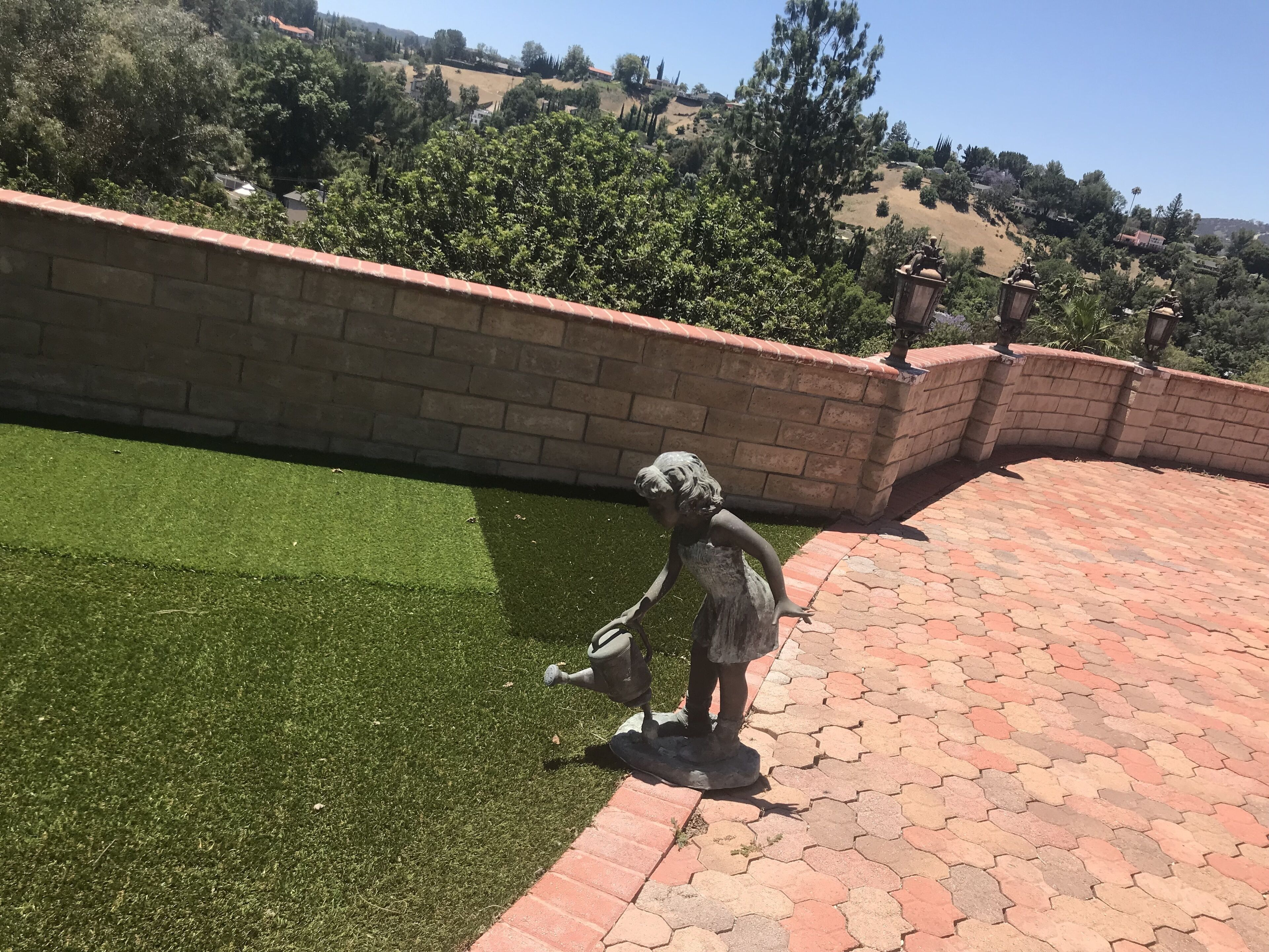 A statue of a figure on a paved area with a brick wall and green grass in the background.