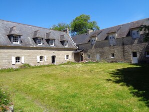 Un bâtiment en pierre doté de nombreuses fenêtres et d’une cour verdoyante.