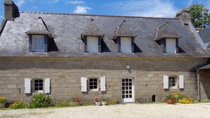 Un bâtiment en pierre doté d’une façade symétrique, de nombreuses fenêtres et d’une allée gravillonnée.