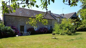 Un bâtiment en pierre avec une cour verdoyante, un barbecue et des sièges extérieurs.