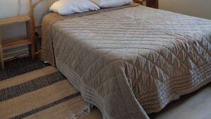 A bed with a wooden frame and a quilted mattress, a wall-mounted light fixture, and a striped rug.