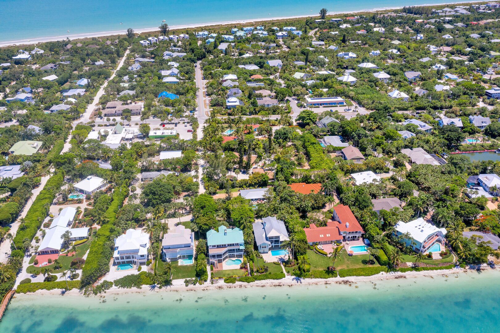 Vista aérea de una zona residencial costera con casas, una playa y aguas azules cristalinas.