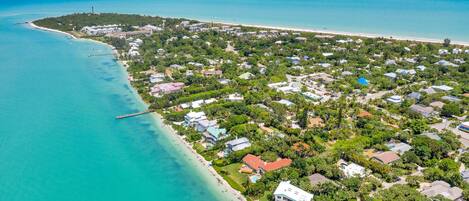 Vista aérea de una zona residencial costera con casas, un muelle y aguas turquesas cristalinas.
