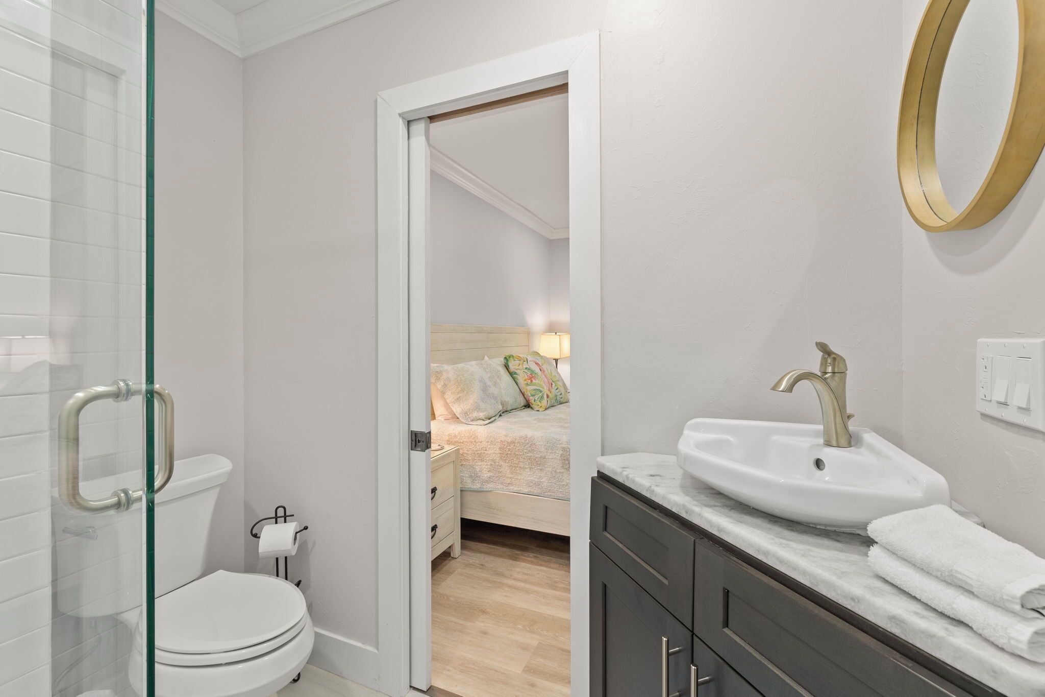 Une salle de bain moderne avec une douche à parois de verre, des toilettes blanches, un lavabo avec un robinet doré et une table de chevet avec une lampe.