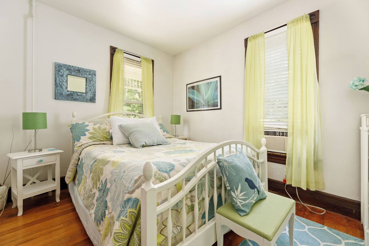 A bedroom with a bed, two bedside tables, a bench, and a window with curtains.